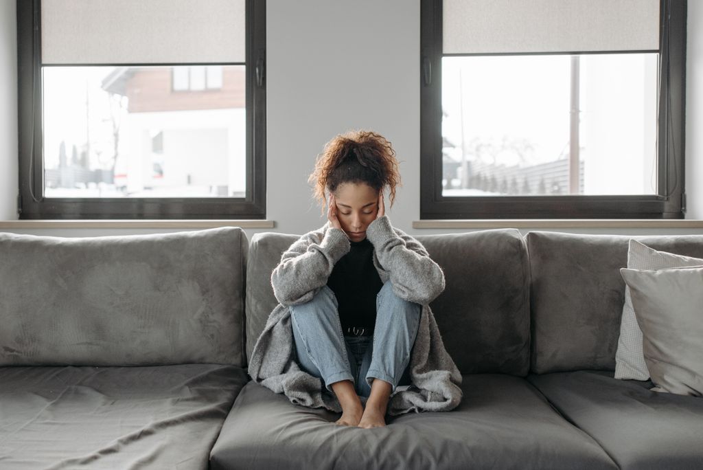 A woman sits on a sofa looking unwell, emphasizing a sense of illness or fatigue indoors.